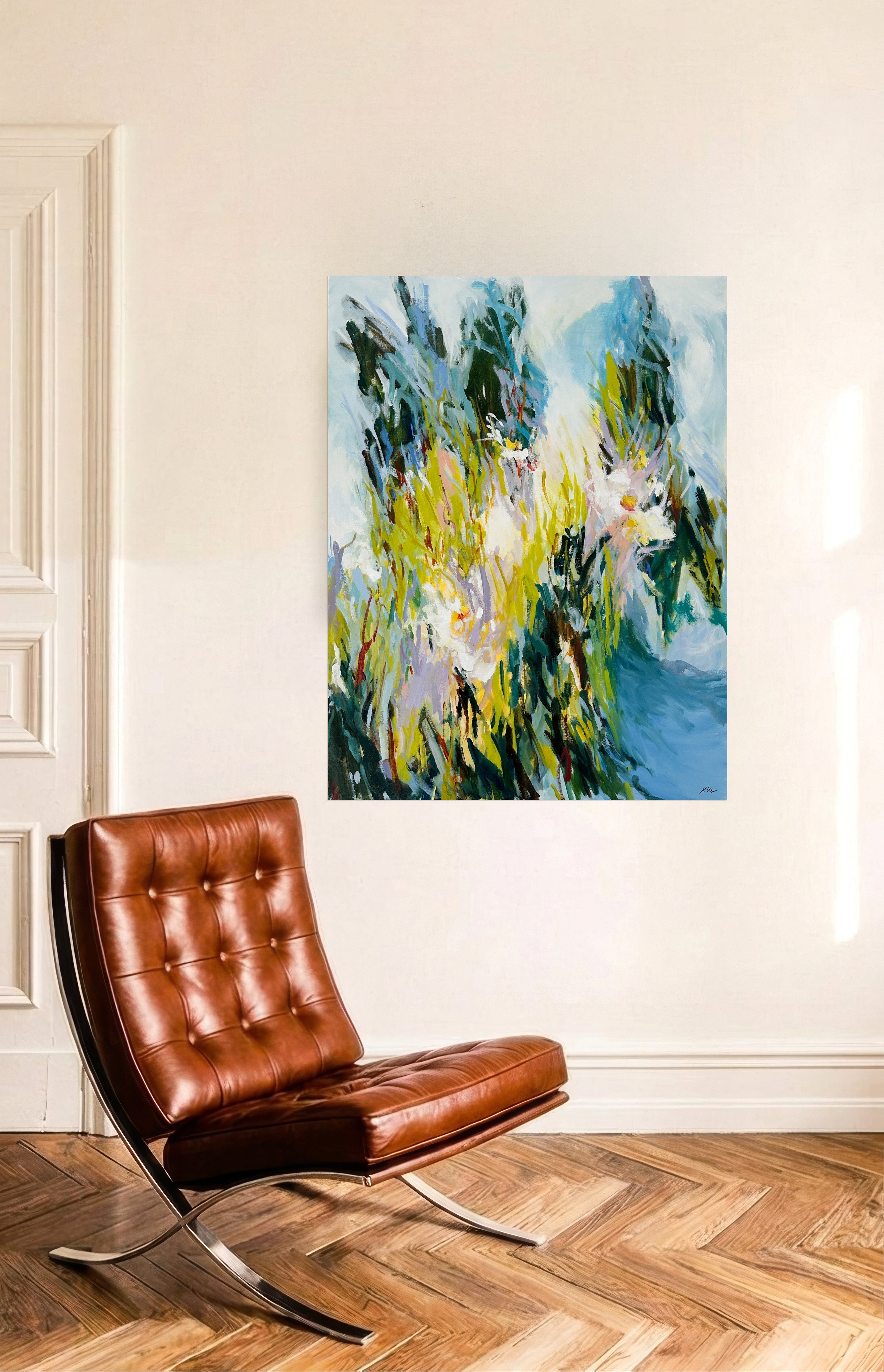 An abstract landscape painting with blue, green, and yellow brushstrokes, displayed on a cream-colored wall above a brown leather chair in a room with a wood herringbone floor.
